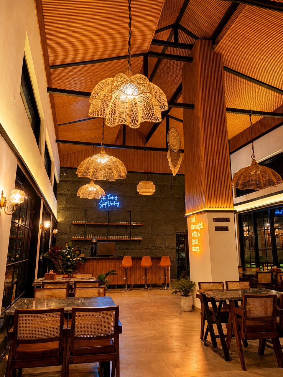 Terrace Café dining room at Tiraya — rattan pendant lights, warm interiors, Stop Thinking Start Drinking neon sign